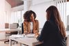 Two female colleagues talking at a desk