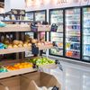 The interior of a convenient store with fresh produce as well as a wall of cold beverages.