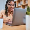 Employee sits at a desk and smiles while working on a laptop. 