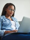 Person in glasses sitting on a couch with a laptop on their lap.