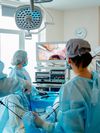 Clinicians wearing scrubs look at a monitor in a clinical setting.