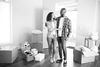 Black-and-white photo of a couple in a barren house with cardboard boxes around them.