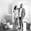 Black-and-white photo of a couple in a barren house with cardboard boxes around them.