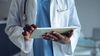 Healthcare clinical professional in white coat and a stethoscope uses a tablet computer.