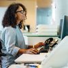 Person in glasses at a desk in an office works at a computer.