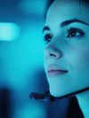 A close-up of a woman wearing a headset, casting a focused expression against a blue-toned background.