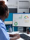 A healthcare professional reviews a reporting dashboard on a desktop computer.