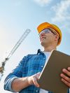 Construction worker in the field, wearing a hardhat and safety glasses while holding a tablet.