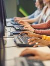 Close-up of hands working on desktop keyboards down a long table.