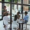 People sit in a conference room with glass walls and windows in an office.