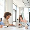 Five colleagues sit in a light-filled modern conference room, happily chatting and working.