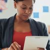 A woman in a blazer and red top looking at a tablet.