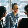 Three young professionals talk together in front of a frosted glass window.