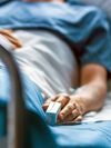 Photo of a patient in a hospital bed with a pulse oximeter on their left hand.