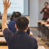 An engaged college or university student raises their hand to ask their professor a question in class.
