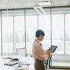 Person in a conference room with tall windows uses a tablet computer.
