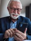 Person with glasses smiles and looks at a mobile phone.