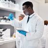 Healthcare lab technician looking at test tube while using a tablet