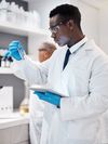 Healthcare lab technician looking at test tube while using a tablet
