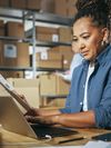 Person works on a laptop in a retail warehouse with cardboard boxes.