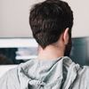 Person wearing hoodie works on dual-monitor desktop computer setup.