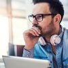 Person with white headphones and holding a tablet computer looks pensive.