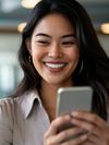 A smiling woman with long dark hair is looking at her smartphone.