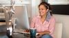 Person sits at desktop computer with coffee mug and decorative flowers in a vase.