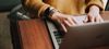 Person wearing mustard-yellow sweater uses a laptop on a wood desk.