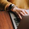 Person wearing mustard-yellow sweater uses a laptop on a wood desk.