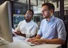Two young professionals collaborate at a desktop computer.